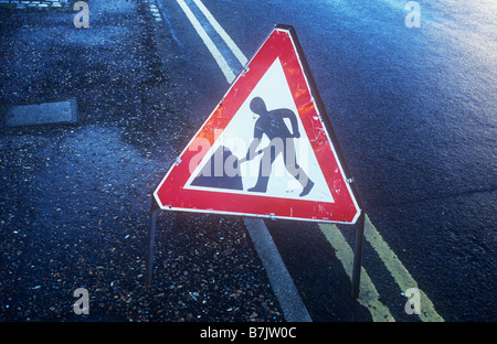 Feuchten sonnenbeschienenen schwarz Straße und Bürgersteig mit roten und weißen Roadworker Schild und gelbe Doppellinien Stockfoto