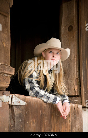 Ein junges Cowgirl, das sich an der Stalltür einer alten Holzscheune in einem Hof lehnt Stockfoto