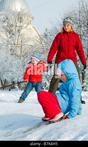 Glückliche Familie (Mutter mit kleinen Jungen und Mädchen) im Winter schneebedeckten Hof in der Nähe von Haus Stockfoto