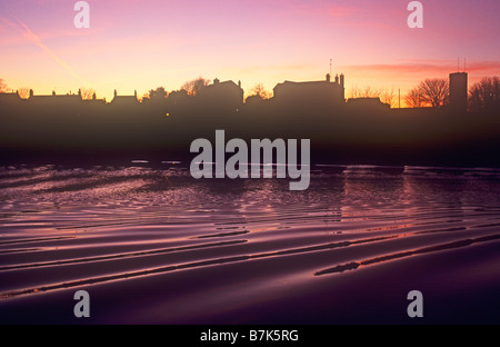 Magenta Sonnenuntergang Himmel spiegelt sich in plätschernden Fluss mit Streifen der Stadtentwicklung in-between Silhouette Stockfoto