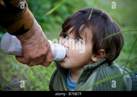 Crawling Baby junge Flasche Fütterung alte Dame mit Flaschengrün Grass als Hintergrund Stockfoto