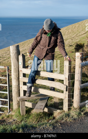 Eine Frau zu Fuß entlang der Ceredigion Coastal Path überqueren einer hölzernen Stil West Wales UK Stockfoto