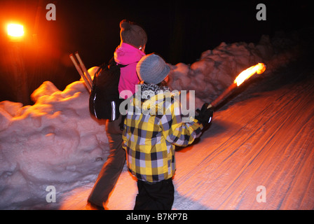 Erwachsene Frau und junge Wandern Tal auf verschneiten Weg von Fackeln beleuchtet Stockfoto