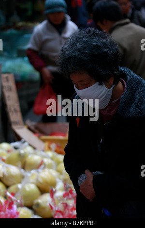 Eine alte chinesische Frau trägt eine Gesichtsmaske während Einkaufen am Markt dies könnte aufgrund der Luftverschmutzung oder die Dtench und Stockfoto