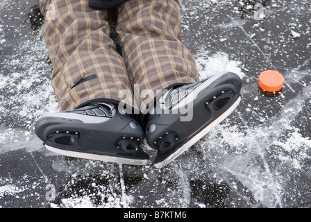 Person mit Schlittschuhen auf zugefrorenen See neben Eishockeypuck, erhöhte Ansicht liegend Stockfoto