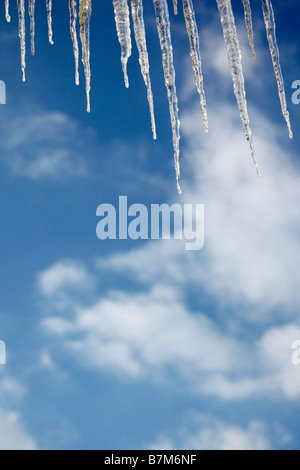 Hängende Eiszapfen auf der Dachrinne auf dem Haus verschwommene Unschärfe Hintergrund blauer Himmel Winterlandschaft Minimalismus minimalistischer künstlerischer minimaler Natur Hi-res Stockfoto