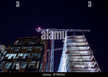 Ein Kran steht hoch zwischen zwei Gebäude auf einer Baustelle in der Nacht in Südost-London, Vereinigtes Königreich. Stockfoto