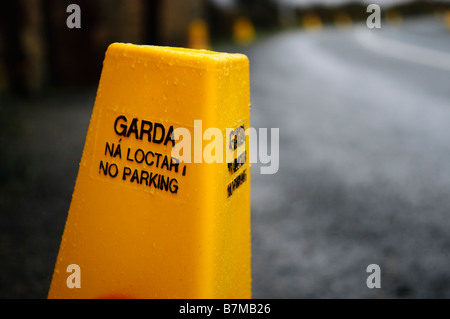 Garda Leitkegel mit zweisprachigen Zeichen in Englisch und Gälisch - gelb "No Parking. Ná Loctar ". Regen und nasser Fahrbahn. Stockfoto