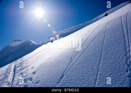 Ski-Alpinisten aufsteigend einen steilen Hang unter einem Gesims in den Schweizer Alpen, Graubünden. Stockfoto