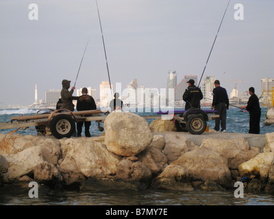 Blick auf die Skyline von Tel Aviv über Männer angeln von einem Pier an der Mittelmeerküste in der Altstadt von Jaffa Hafen. Israel Stockfoto