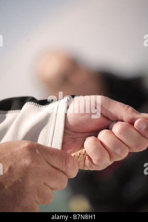 Nahaufnahme eines Mannes mit einem Seil auf einer Yacht mit einem anderen Segler im Hintergrund unscharf. Stockfoto