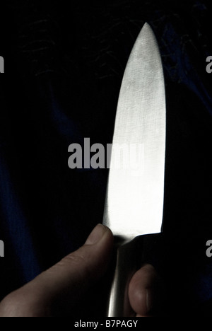 Die Hand eines Mannes mit einem glänzenden Metall Messer gegen einen dunklen Hintergrund. Stockfoto