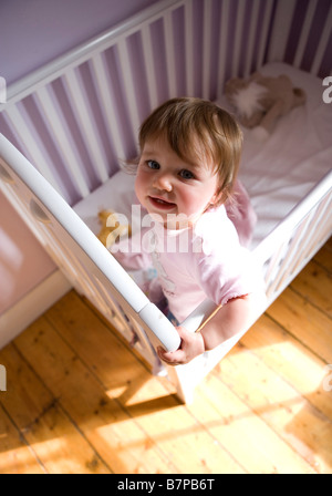 Ein elf Monate altes Babymädchen setzt sich in ihrem Kinderbett. Stockfoto