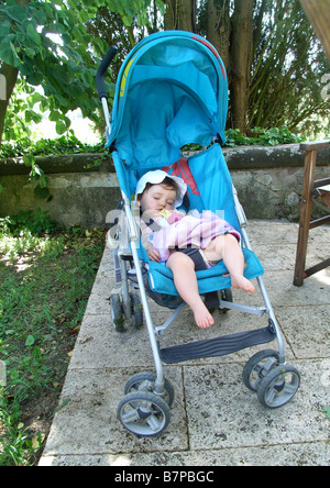 Ein Mädchen liegt im Schatten während eines Urlaubs in ihrem Kinderwagen schlafen. Stockfoto