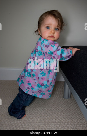 Ein acht Monate altes Babymädchen zieht sich bis um zu stehen. Stockfoto