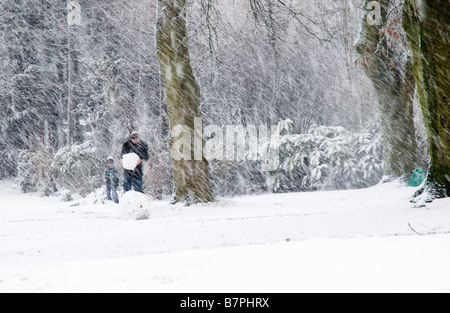 Vater und Sohn spielen zusammen in einem Park machen einen Schneemann im Schneesturm Stockfoto