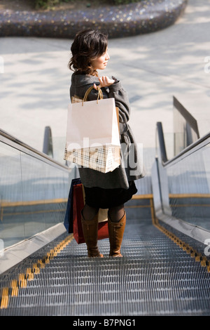 Junge Frau Einkaufstaschen Seitenansicht Rolltreppe hinunter Stockfoto