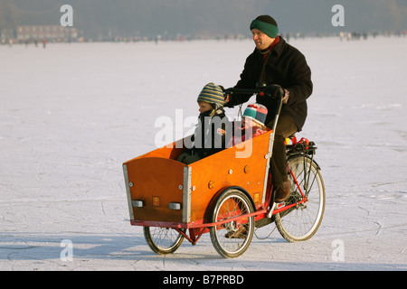 Mann in schwarzer Jacke Radfahren mit Kindern auf Eis gefroren Kralinger See Winter Niederlande Rotterdam Stockfoto
