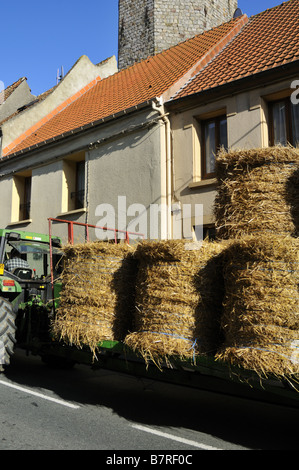 Ein Traktor zieht einen Anhänger Ladened mit runder Heuballen durch die Pas-de-Calais Stadt Samer, Frankreich. Stockfoto