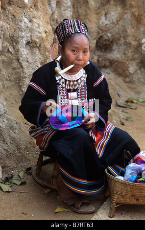 Akha Hill Tribe Frau im traditionellen Kleid Rauchen & nähen, Provinz Chiang Mai, Nordthailand Stockfoto