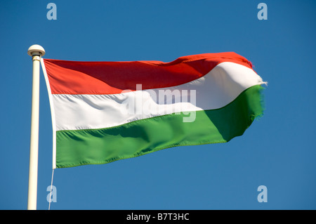 Ungarische Flagge, die an einem sonnigen Tag von einem weißen Fahnenmast aus fliegt. Vor einem klaren blauen Himmel gesehen. Stockfoto