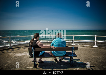 Weißer Mann und Frau, von hinten gesehen, auf einer Bank, am Meer bei Aberystwyth mit Blick auf den blauen Himmel und das türkisfarbene Meer Stockfoto