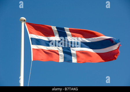 Norwegische Flagge, die an einem sonnigen Tag von einem weißen Fahnenmast aus fliegt. Vor einem klaren blauen Himmel gesehen. Stockfoto