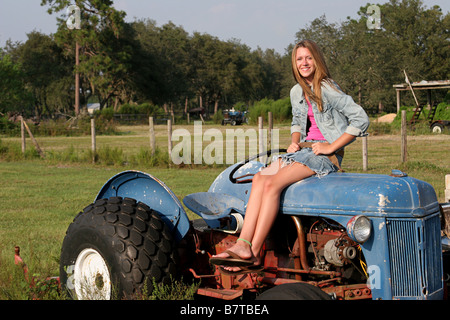Eine schöne blonde Mädchen sitzen auf einem Traktor in der Mitte einer farm Stockfoto