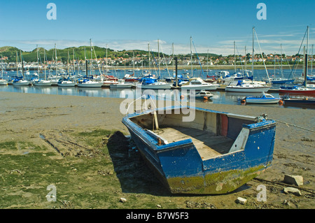 Alte blaues Boot gezogen bis zum Strand in Conwy mit vielen Booten und Yachten vertäut am Fluss hinter Stockfoto