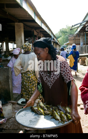 Arbeitnehmerin trägt ein Tablett mit ausgenommene gelber Fisch in einem nigerianischen Fischmarkt Stockfoto