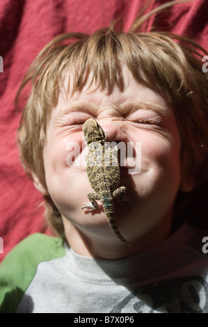 sechs Jahre alter Junge mit Haustier Bartagame Klettern auf seinem Gesicht Stockfoto