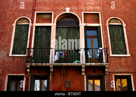 Grünen Türen und Fensterläden hinter einem Balkon in Venedig Italien gegen eine helle Rost farbigen Wand gesetzt. Stockfoto