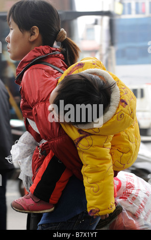 Chinesische Migranten Frau mit ihrem Baby auf dem Rücken am Bahnhof von Nanchang, Jiangxi Provinz, China. 5. Februar 2009 Stockfoto