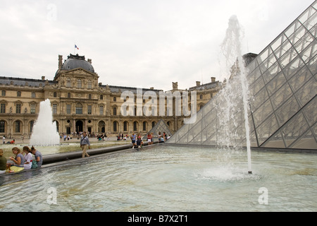 Menschen sitzen vor dem Louvre-Pyramide und Brunnen an einem bewölkten Tag Stockfoto