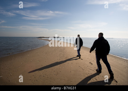 Eine Doppelbelichtung zeigt einen Mann zu Fuß entlang einer Sandbank in Richtung einer Insel mit dem Ozean Stockfoto