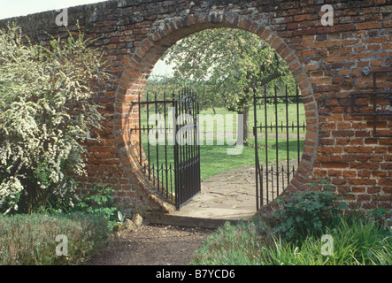Lullingstone Kent UK Schmiedearbeiten Mond Tor in der Mauer, die im Frühjahr blühen im Obstgarten jenseits gesehen Stockfoto