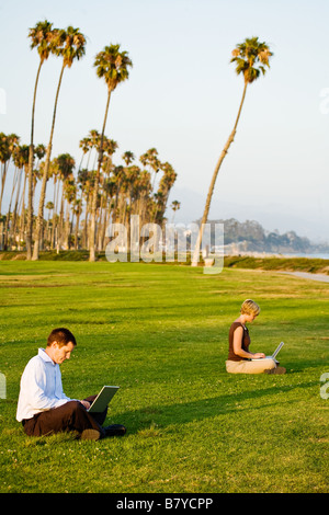 Ein modernes Paar soziale Distanzierung auf ihren Laptop-Computern draußen in einem Park. Stockfoto