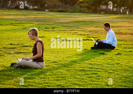 Ein modernes Paar soziale Distanzierung auf ihren Laptop-Computern draußen in einem Park. Stockfoto