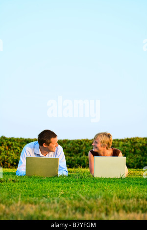 Eine moderne Fernbedienung für ein Paar, die draußen in einem Park auf einem Laptop arbeitet. Stockfoto