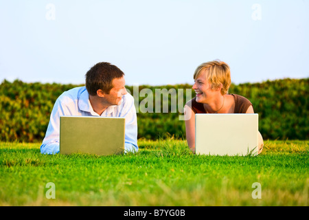 Eine moderne Fernbedienung für ein Paar, die draußen in einem Park auf einem Laptop arbeitet. Stockfoto