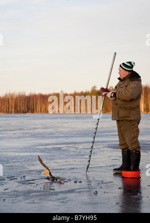 Älterer Mann mit einem Eis sah ein Loch ins Eis um zu prüfen, Fischernetze, Finnland öffnen Stockfoto