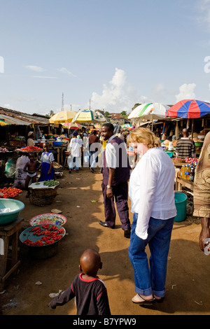 Weiße Frau geht durch einen nigerianischen Markt an einem heißen sonnigen Tag und lächelt ein kleiner Junge Stockfoto