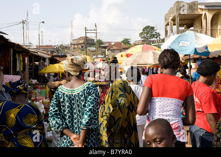 Nigerianische Volk zu Fuß durch ein lokales Dorf in Poka, Epe, mit ihrem schlechten Dorf in der Ferne Stockfoto