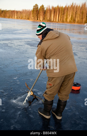 Älterer finnischer Mann, der mit einer Eissäge ein Loch in das Eis sägt, um Netze zu fischen, Finnland Stockfoto