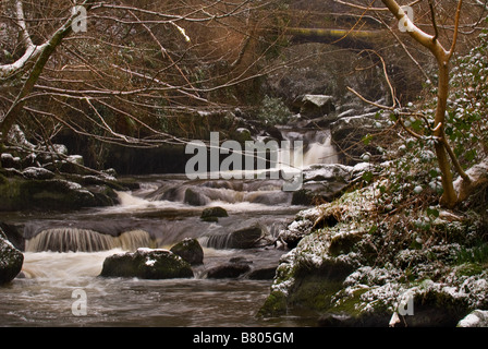 Ein kleiner Fluss läuft durch ein bewaldetes Tal im Winter. Stockfoto