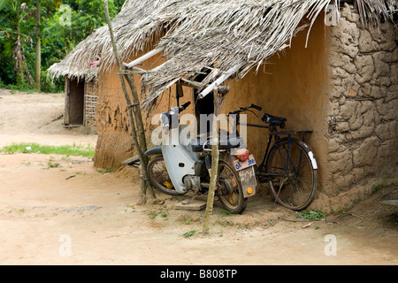 Altes Fahrrad schieben und eine Honda Scooterette lean unter Schutz gegen ein Flechtwerk und Lehm-Haus in einem abgelegenen Dschungel Dorf von Nigeria Stockfoto