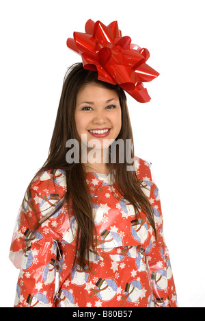 Eine junge asiatische Frau lächelt, als sie in Weihnachts-Geschenkpapier eingewickelt ist und garniert mit einer großen roten Schleife Stockfoto