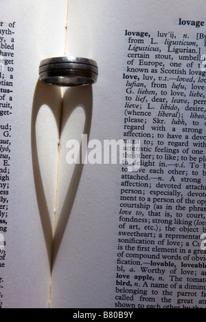 Nahaufnahme von einer herzförmigen Schatten vom Licht fällt auf einen Ehering neben Worte über die Liebe in einem Wörterbuch Stockfoto