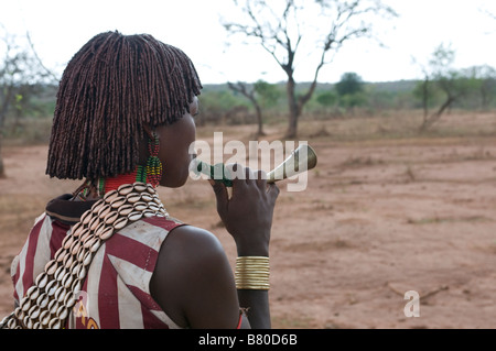 Junge Hamer Mädchen bläst ein Horn um Männer zu gewinnen, während das Springen der feierlichen Bull Äthiopien Afrika Stockfoto