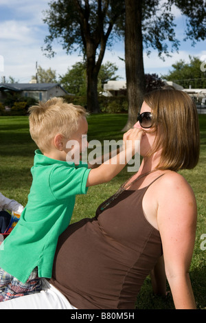 Vorschulalter Jungen spielen mit schwangere Mamas Nase und Sonnenbrille im Freien im park Stockfoto